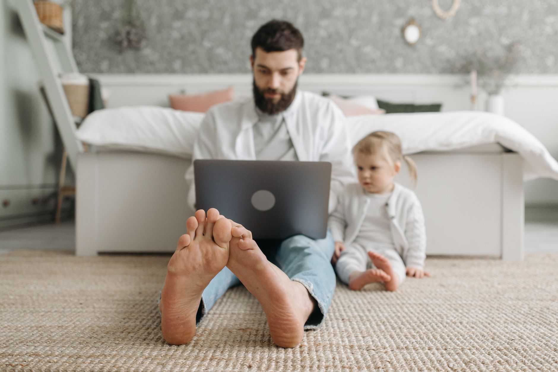 A parent working at a laptop with a nursery visible in the background.