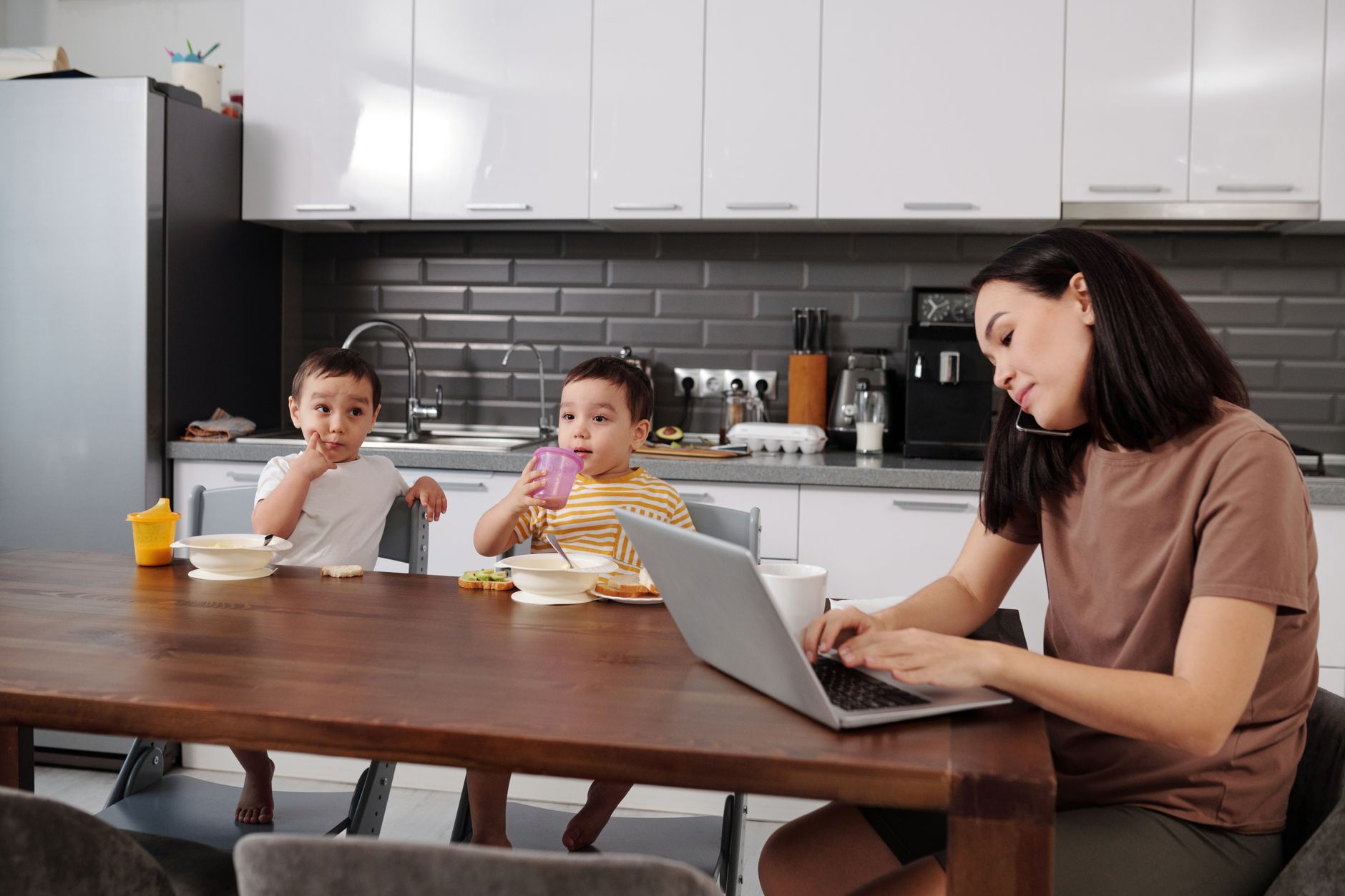 A parent using a laptop in a busy family kitchen environment.