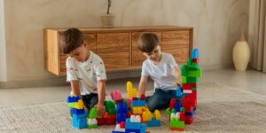 Two children building blocks together in a sunlit room.