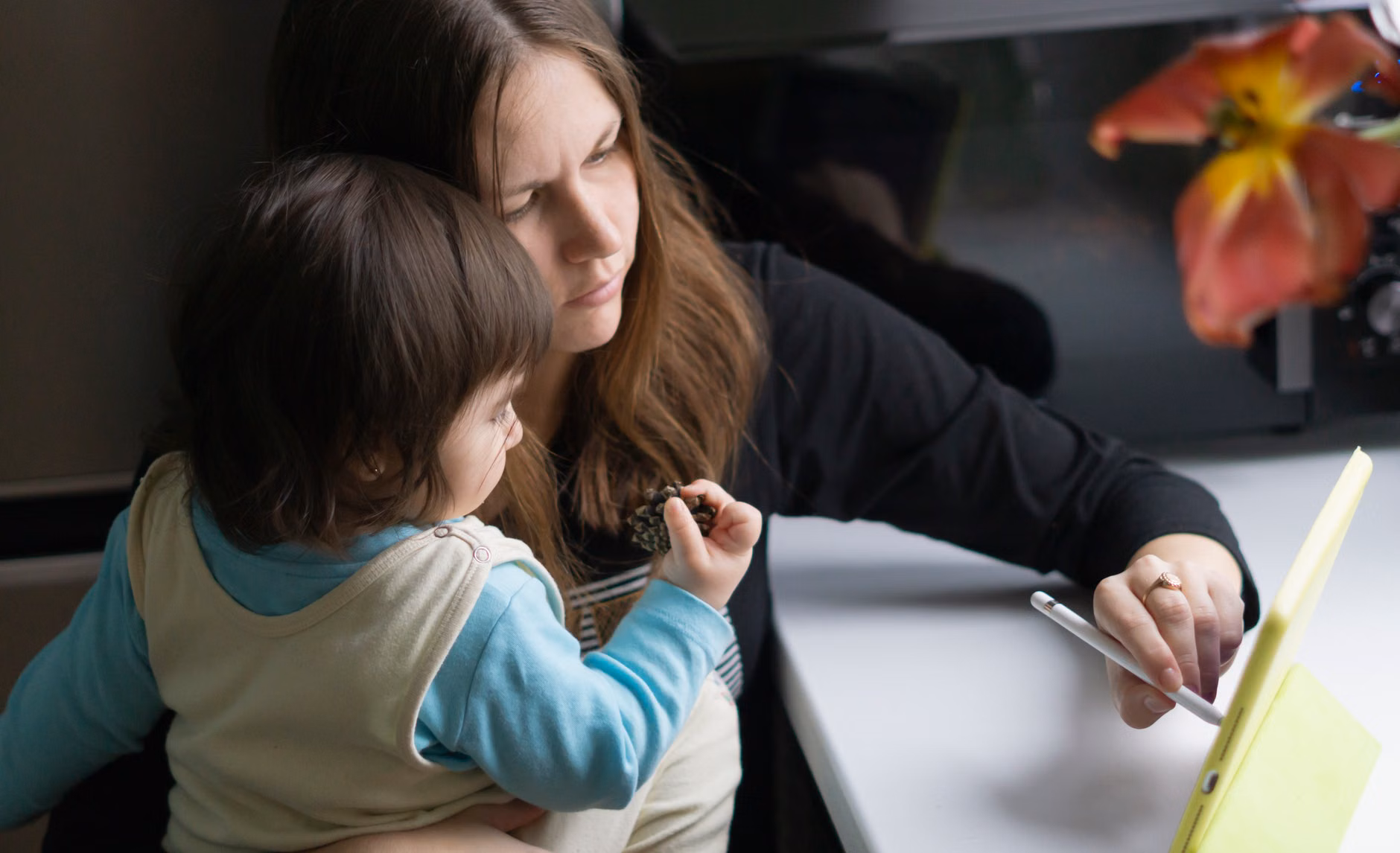 A parent and child using a tablet together at a dining table.