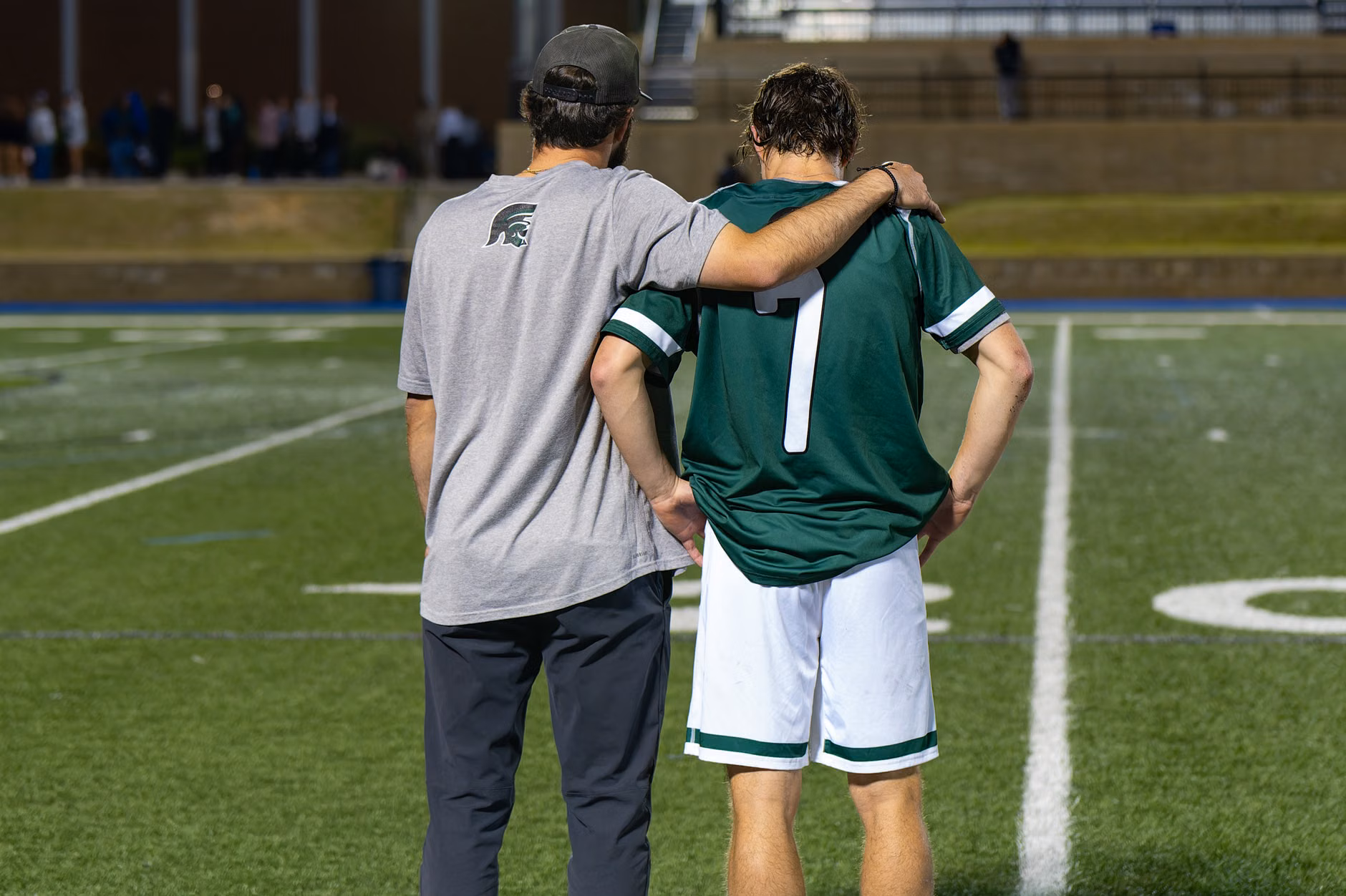 A coach mentoring a young athlete on a sports field.