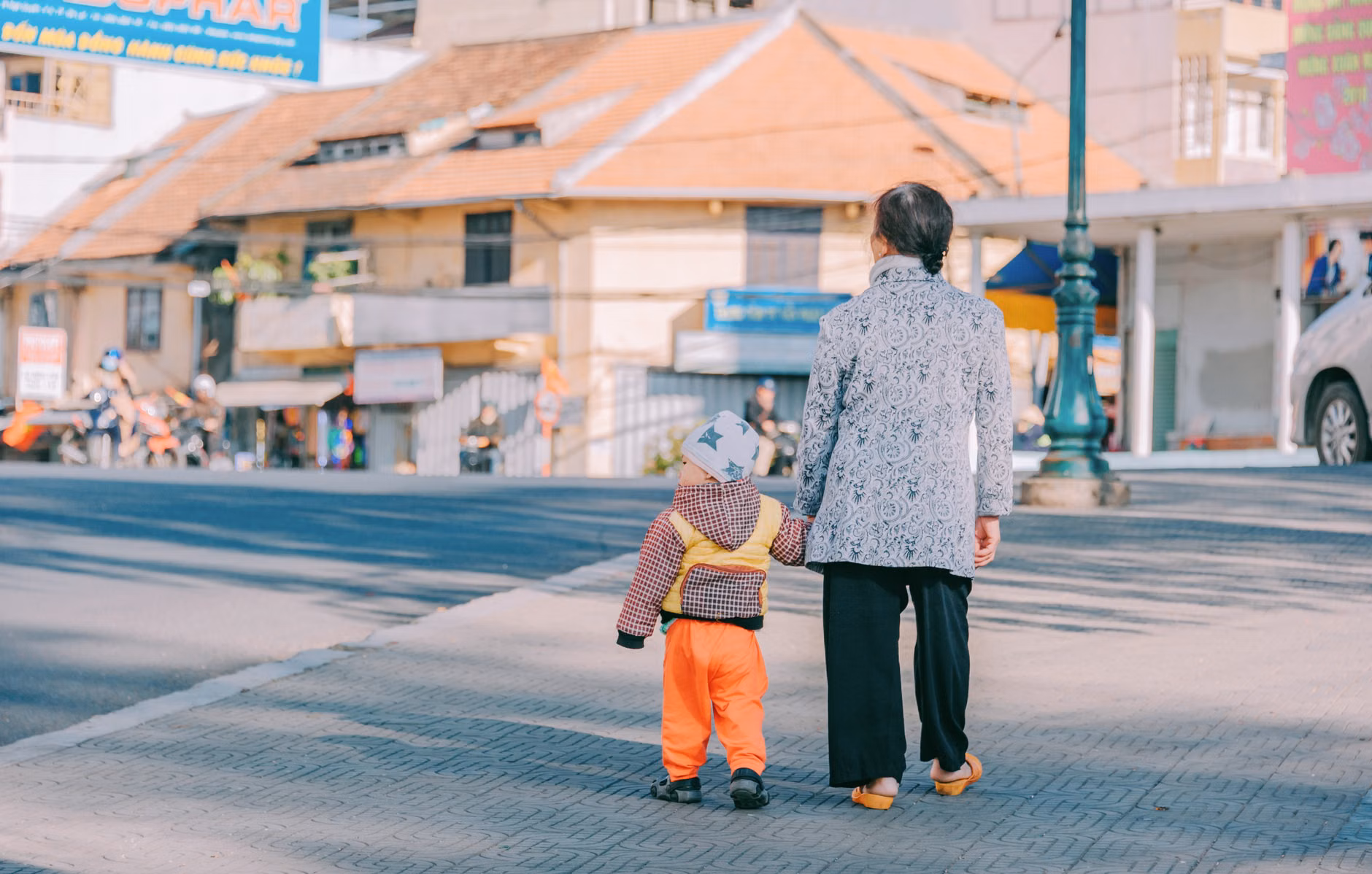 An elderly person and a child walking together on a flat path.