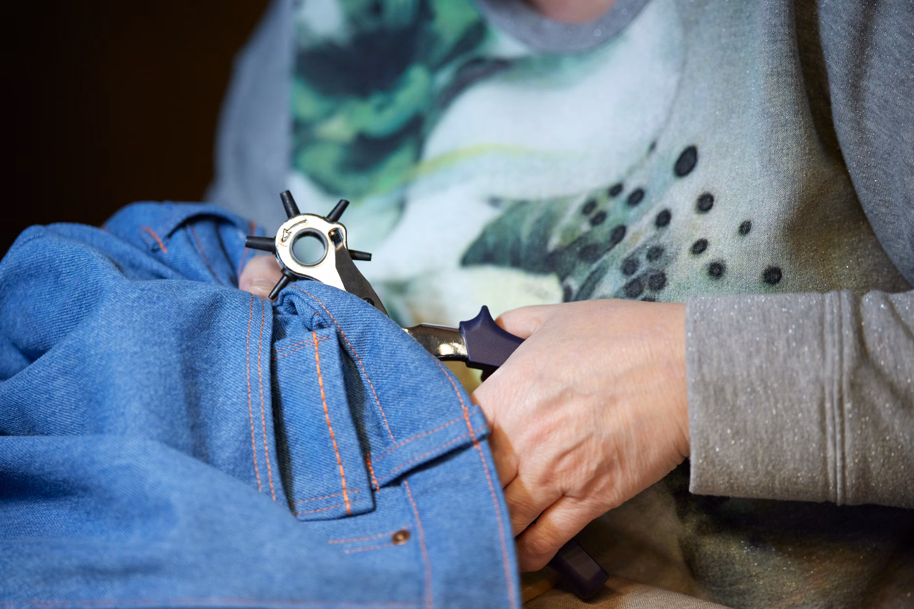 A professional tailor repairing a pair of denim jeans.