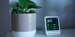 A sleek smart air quality monitor on a bedside table in a sunlit room.