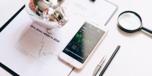 A smartphone with a finance app next to a piggy bank on a kitchen table representing digital financial literacy.