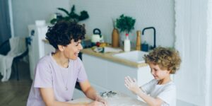 A child and parent baking together in a sunlit kitchen, focusing on measuring ingredients.