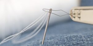 A pair of mended jeans with visible stitching next to sewing tools on a wooden surface.