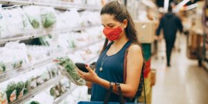 A parent checking a smartphone in a grocery store with digital price tags on the shelves.