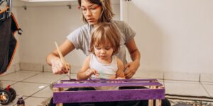 A parent and child building a birdhouse together in a sunny garden, representing slow-schooling.