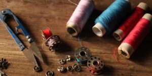 A sewing kit and mending project on a wooden table, representing the slow-fashion movement.