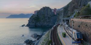 A modern train traveling along a scenic coastline during sunset.