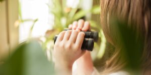 A person using binoculars in a peaceful suburban garden setting.