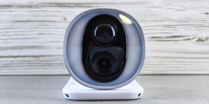 A sleek smart home camera placed on a bookshelf in a modern rental apartment.