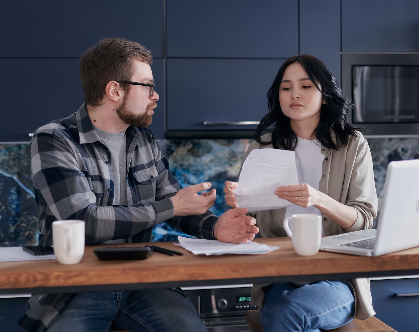 A parent relaxing at a kitchen table while managing finances digitally.
