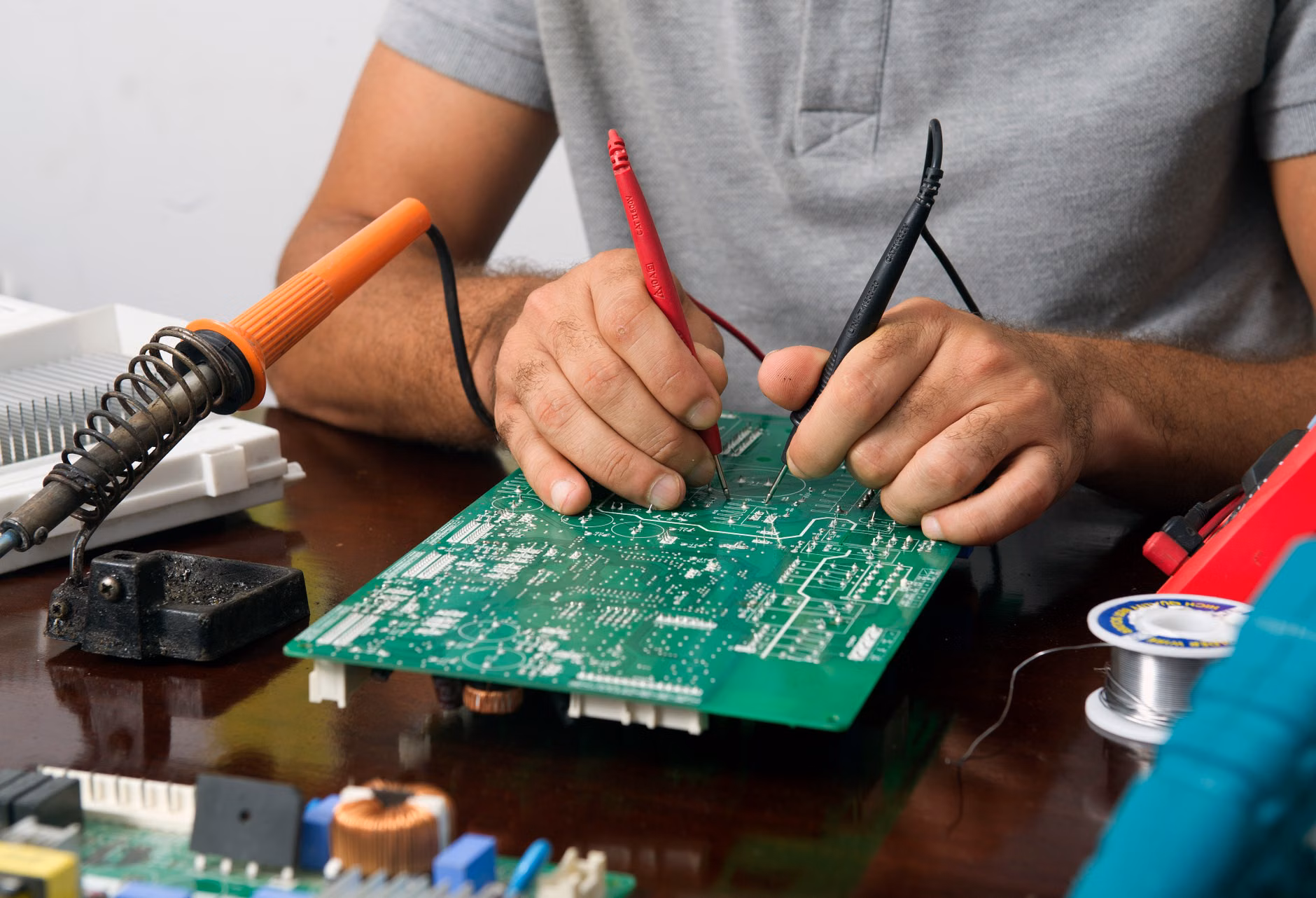Hands testing an appliance component with a digital multimeter.