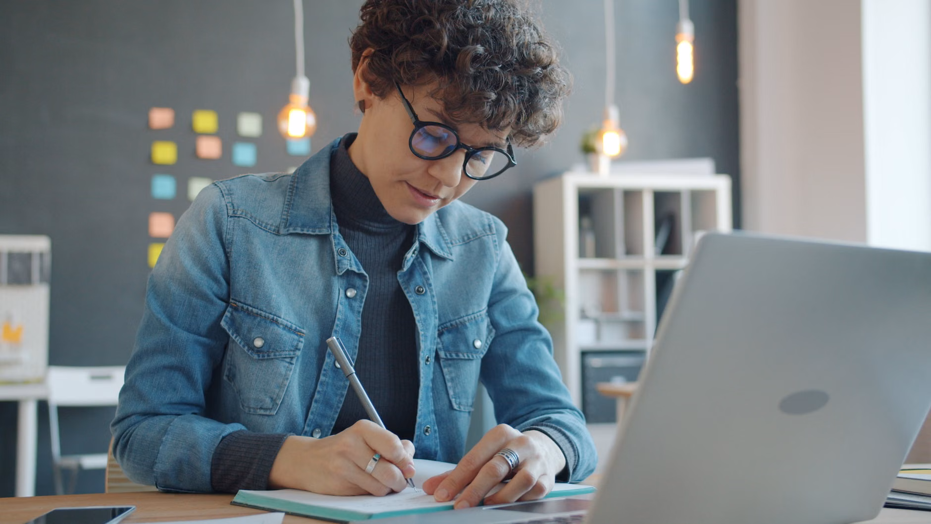A person performing a cognitive-load audit by writing down tasks in a notebook.