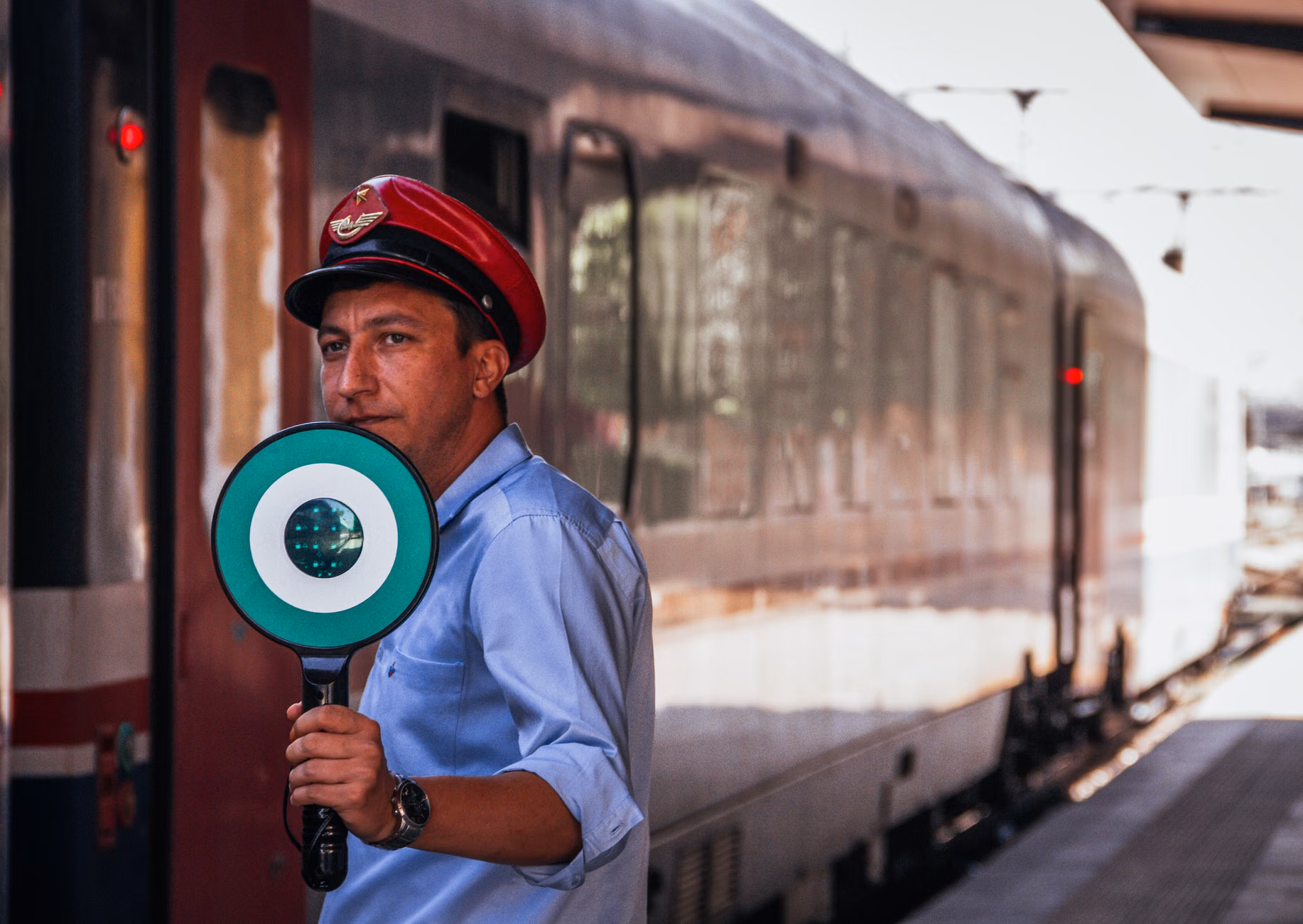 A train conductor on a historic railway platform checking a pocket watch.