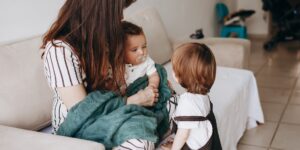 A parent observing two children on a sofa, representing a calm approach to sibling conflict.