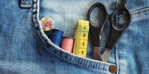 A organized sewing kit and a pair of jeans needing repair on a wooden table.