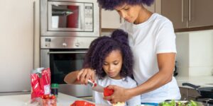 A parent and child preparing food together in a calm, warm kitchen setting.