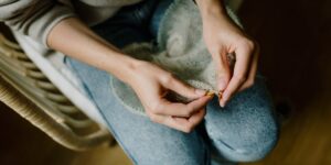 A close-up of hands mending a wool sweater to represent the slow fashion movement.