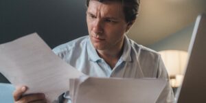 A focused remote-working parent reviewing financial documents at a home office desk.
