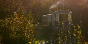 A scenic view of a vintage steam train traveling through a lush mountain valley at sunset.