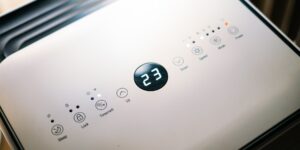 A sleek, modern smart home air quality sensor on a shelf in a brightly lit, minimalist living room.