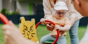 A parent and toddler rearranging modular outdoor play equipment in a backyard.
