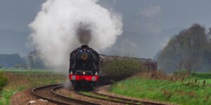 A scenic view of a vintage steam train traveling through a vibrant, lush mountain valley during autumn.