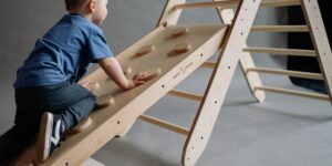 A toddler playing on a modular wooden outdoor climbing set in a sunny backyard.
