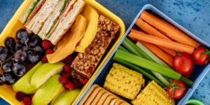 A balanced, colorful school lunchbox featuring a mix of international snack foods on a wooden table.