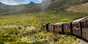 A vintage steam train traveling through a scenic valley during golden hour.