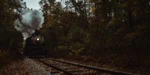 A vintage steam train traveling through a colorful autumn forest.