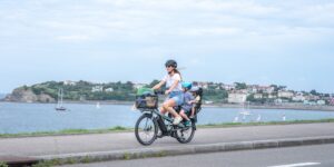 A parent cycling with children on a cargo bike on a sunny city bike path.