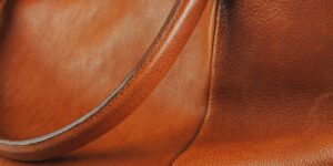 Professional artisan restoring a vintage luxury leather handbag on a wooden workbench.