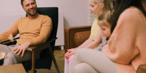 A parent calmly facilitating a conversation between two children in a small, modern living space.