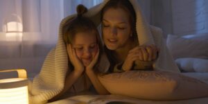 Parent and child reading a book together in a warm, cozy living room.