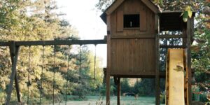 A modular wooden climbing structure in a backyard setting designed for adaptive play.