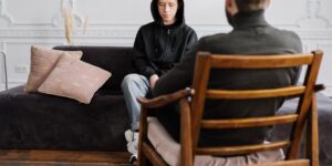 A parent and teenager sitting on opposite ends of a sofa in a modern living room.