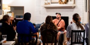 A group of new fathers meeting in a living room to discuss parenting experiences.