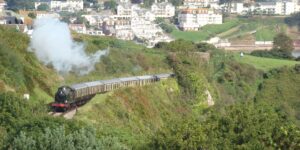 A scenic heritage steam train journeying along a beautiful coastline at sunset.