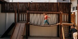 Children playing on a natural wooden climbing structure in a forest playground.
