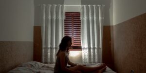 A calm parent sitting in a dimly lit, minimalist bedroom while a toddler rests.